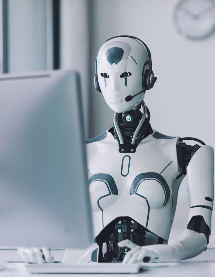 Android AI robot sitting at the desk and working in the office: artificial intelligence, business and automation concept