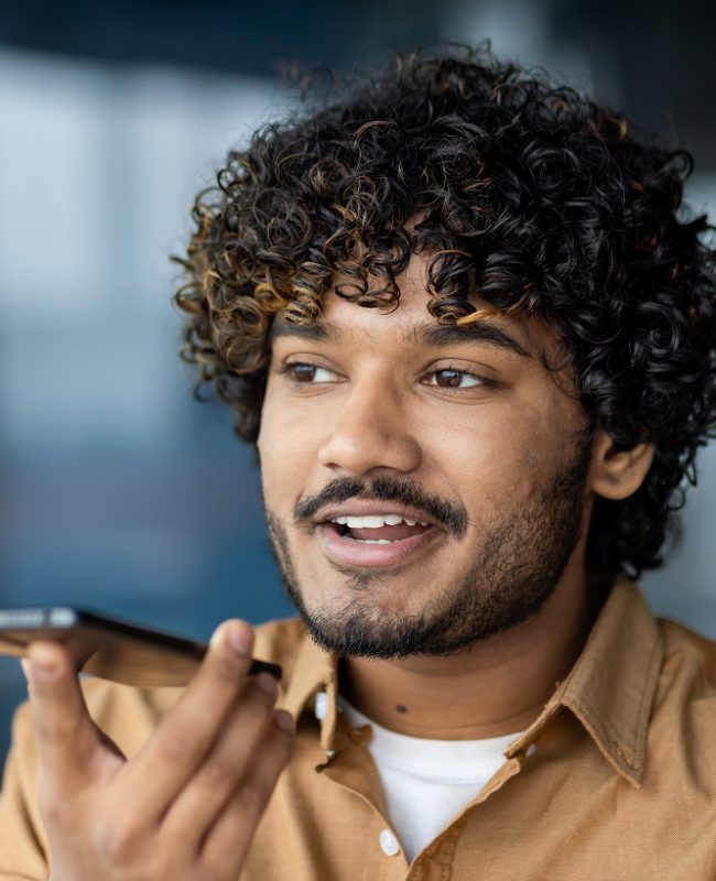 Close-up of a young male businessman using an application on a smartphone to record an audio message, a boss in a shirt, dictating commands, and recording notes on a voice recorder.
