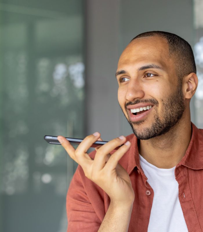 Smiling man using smartphone for voice call in modern office. Casual attire, expressing joy, connectivity. Professional, relaxed setting. Technology and communication theme.